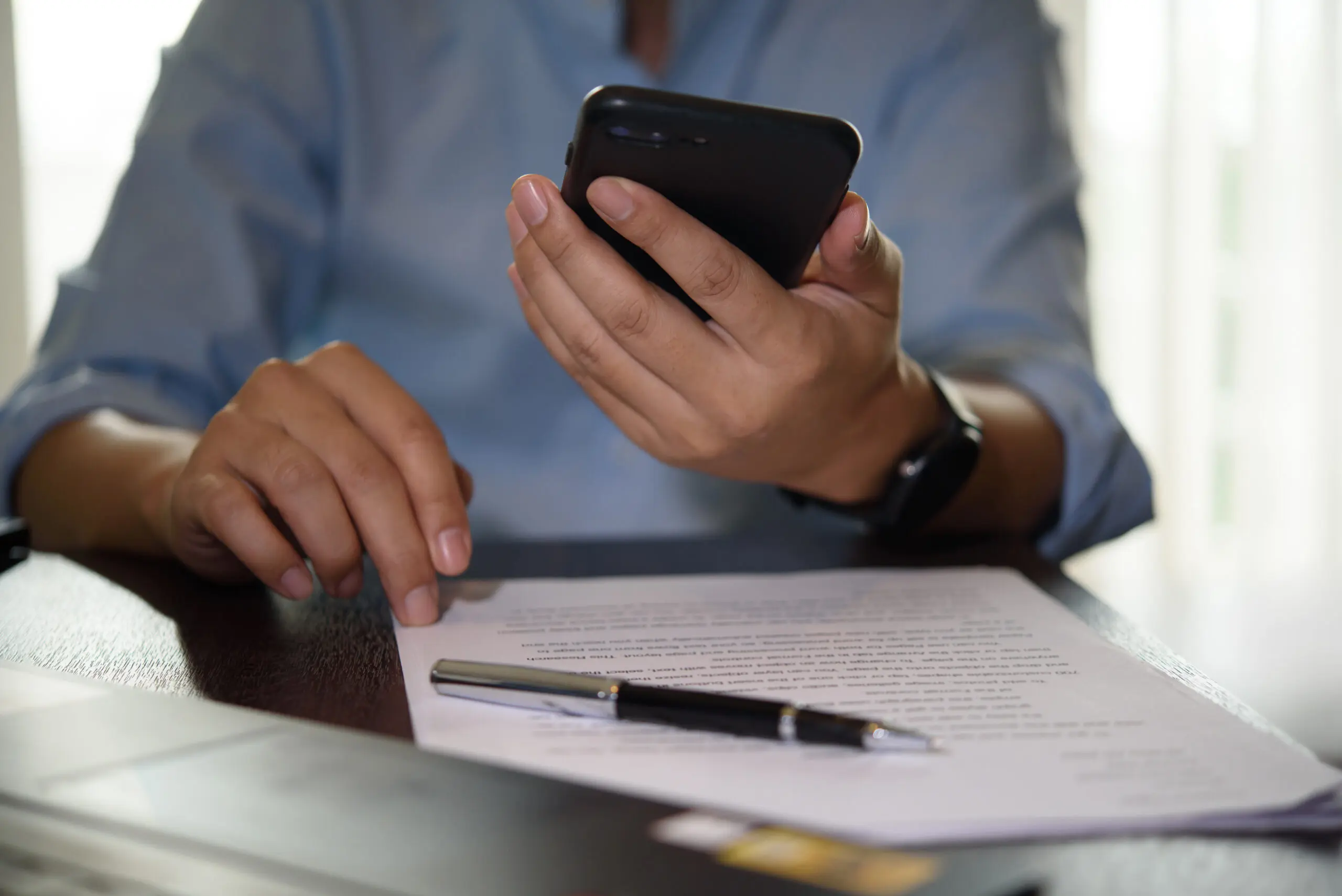 Hand holding smartphone while reviewing paperwork